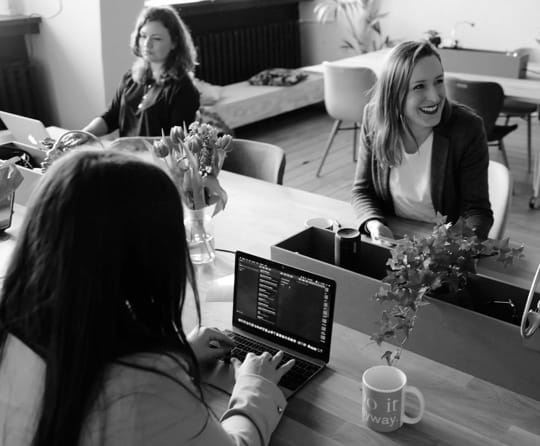 a young lady on her laptop, with her colleagues sharing a desktop together