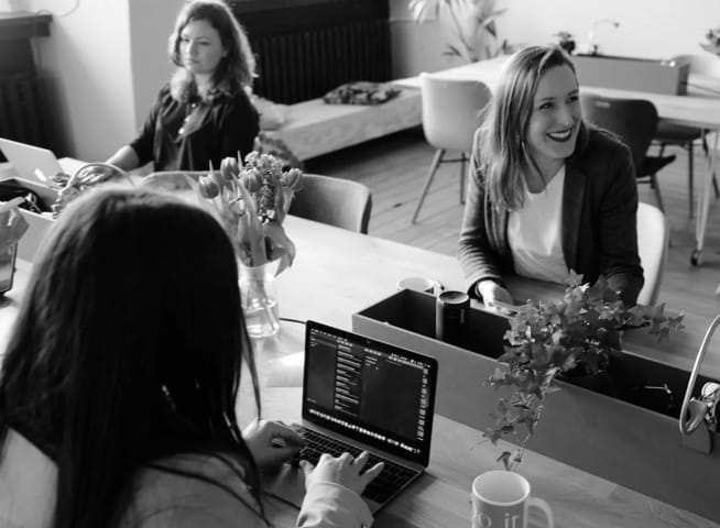 a young lady on her laptop, with her colleagues sharing a desktop together